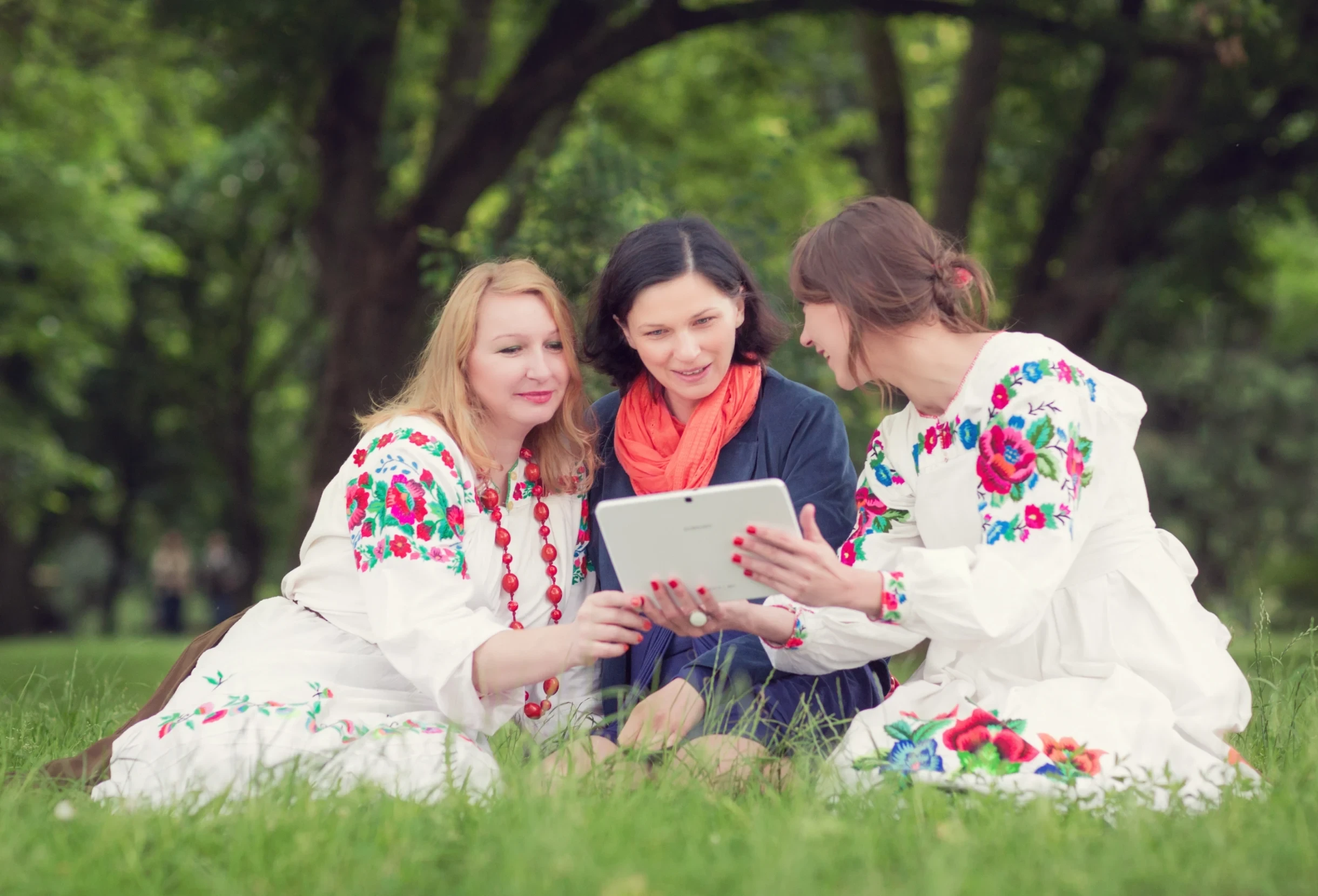 Trzy kobiety wspólnie korzystają z tabletu w plenerze